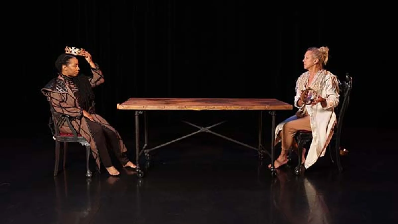 Two dancers seated at a table on a stage. 