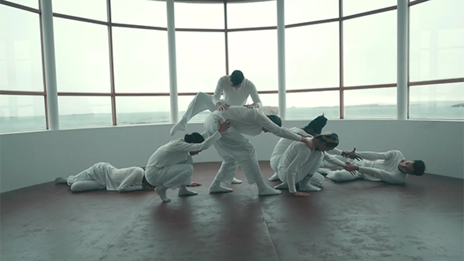 Dancers dressed in white in front of a large window